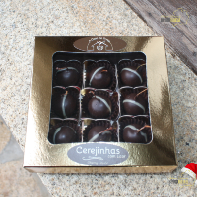 Caixa dourada com cerejas cobertas de chocolate em forminhas pretas sobre granito