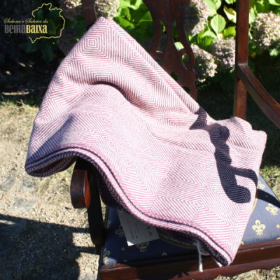 Manta rosa com padrão geométrico sobre cadeira de madeira numa área exterior