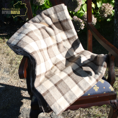 Manta xadrez creme e castanha sobre cadeira de madeira escura com almofada azul num jardim