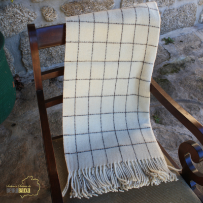 Manta bege com padrão xadrez e franjas numa cadeira de madeira