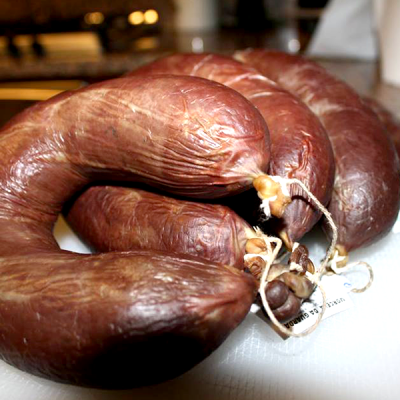 Quarteto de enchidos curados castanhos escuros com cordão amarrado sobre superfície branca