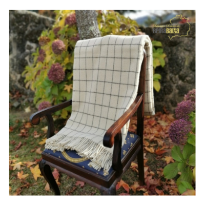 Mantinha bege com padrão quadriculado azul numa cadeira de madeira escura com estofado azul no jardim