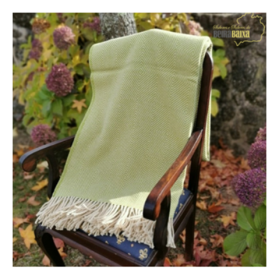 Manta verde clara com padrão em zigzag e franjas sobre cadeira de madeira com almofada azul em jardim outonal