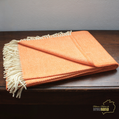 Manta laranja com franjas brancas sobre madeira escura com logo Beira Baixa