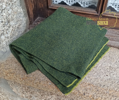 Manta ou xale verde tecido dobrado sobre pedra junto a janela de madeira