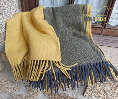 Manta amarela e cinzenta com franjas sobre pedra e madeira perto de uma janela