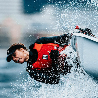 Homem com colete salva-vidas vermelho e preto inclinado fora do barco com água a espirrar
