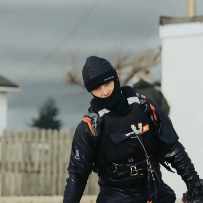 Pessoa com fato negro e colete 'ROGUE' ao ar livre com vedação branca e céu nublado ao fundo