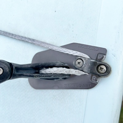 Peça metálica cinza com parafusos e corda branca trançada em superfície branca