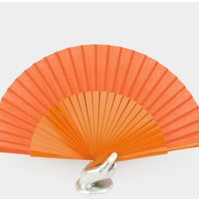 Leque laranja apoiado em mão prateada contra fundo cinza claro