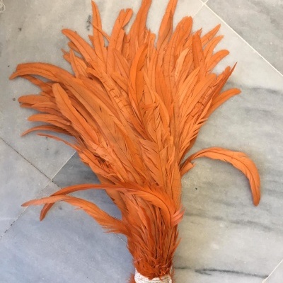 Pena decorativa laranja amarrada na base com corda branca sobre mármore cinza