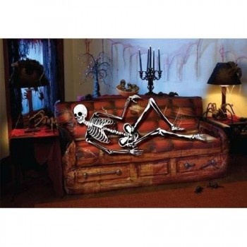 Sofá marrom com esqueleto branco deitado e decoração de sala com lâmpada e suporte de velas