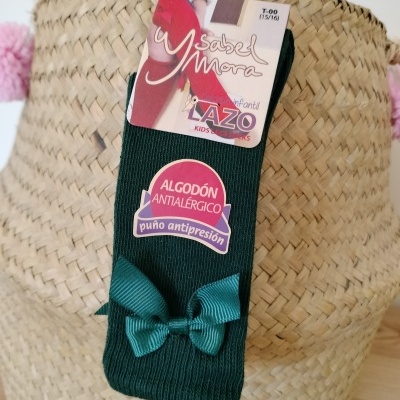 Meia verde escura infantil com laço e etiqueta Ysabel Mora sobre cesta de palha
