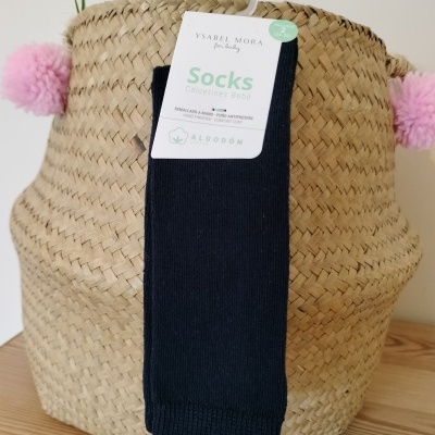 Meias pretas para bebé da marca Ysabel Mora com etiqueta penduradas numa cesta de vime com pompons cor de rosa