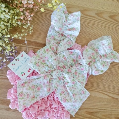 Roupa de bebé rosa com laço floral e etiqueta Sara Pinto sobre madeira