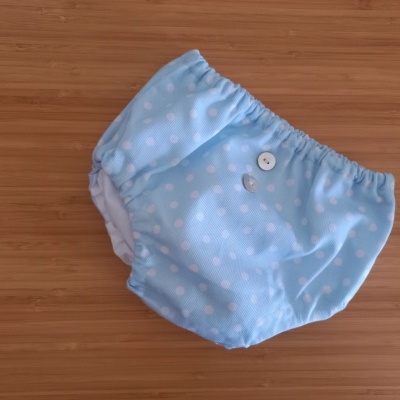 Fralda reutilizável azul clara com padrão branco de pequenos círculos e botões