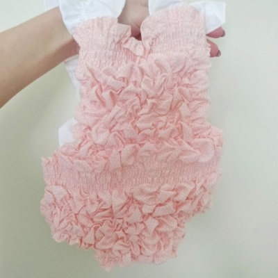 Roupa infantil rosa com textura franzida e babados, alças brancas com folhos.