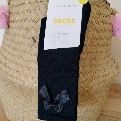 Meia infantil preta com laço e etiqueta Ysabel Mora sobre cesto de palha.