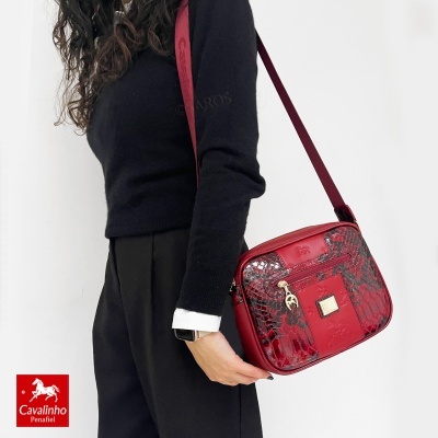Mala vermelha com padrão pele de cobra e detalhes dourados, usando alça de ombro, em fundo branco.