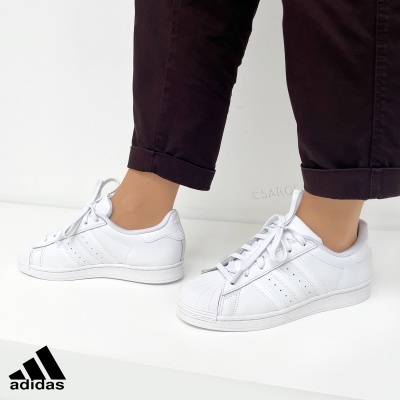Tênis Adidas Superstar brancos usados com calças pretas