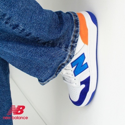 Ténis multicoloridos New Balance com calças de ganga azul contra uma parede branca