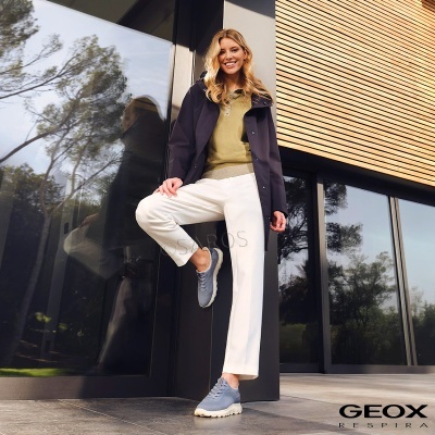 Mulher com roupa casual e ténis cinzentos junto a edifício moderno com vidro e madeira