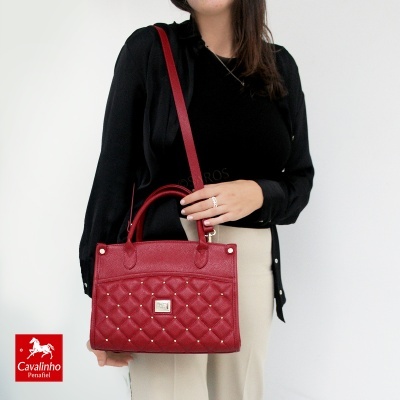 Mulher segura mala vermelha matelassê com alça vermelha, fundo branco e logótipo Cavalinho Penafiel
