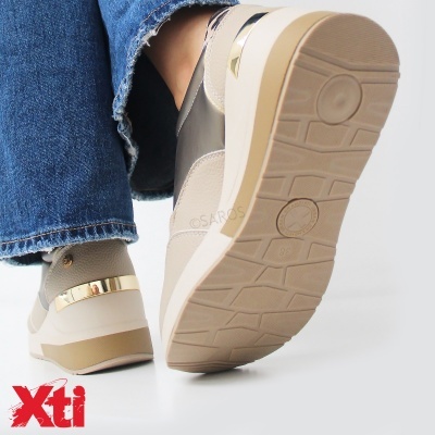 Ténis bege com sola antiderrapante e detalhe dourado usados com calças de ganga azuis