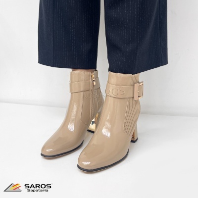 Botins bege de verniz com salto alto e fivela, calças azuis e fundo branco