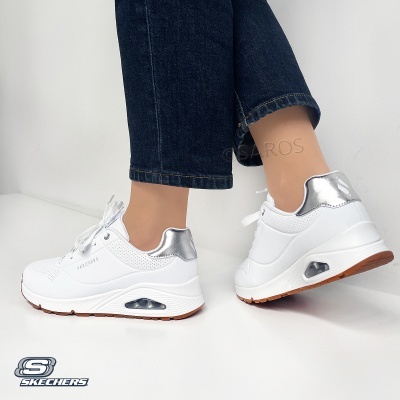 Ténis Skechers brancos com detalhes prateados e sola castanha usados com calças de ganga