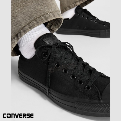 Ténis Converse pretos de lona com atacadores pretos e sola preta usados com meias brancas.