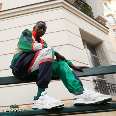 Homem com fato de treino colorido e sapatilhas brancas sentado num banco verde ao ar livre