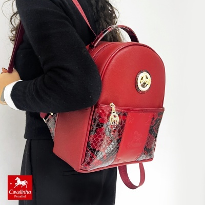 Mochila vermelha de pele com detalhes em padrão de pele de cobra usada por uma pessoa vestindo preto