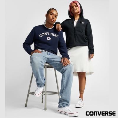 Dois modelos com roupa Converse azul escuro, preta, jeans claros e ténis brancos em fundo branco.