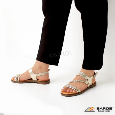 Sandálias douradas com tiras trançadas e fivela ao lado em fundo branco