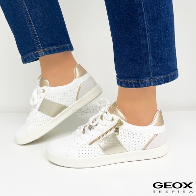 Tênis brancos com detalhes dourados e zíper lateral usados por pessoa com jeans azul