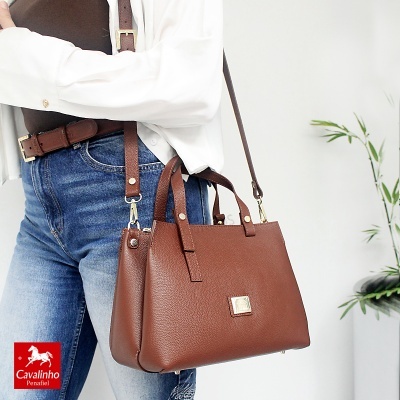 Mala castanha de pele com alças e tiracolo, usada por pessoa com roupa casual
