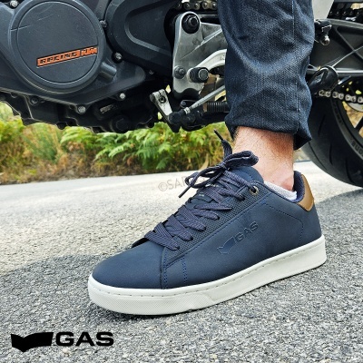 Ténis masculinos azuis com sola branca e detalhe castanho usados ao lado de mota preta