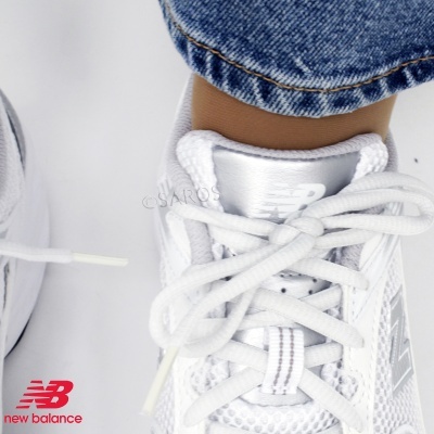 Ténis New Balance brancos com cadarços e detalhes em tecido mesh, calças de ganga azul claro