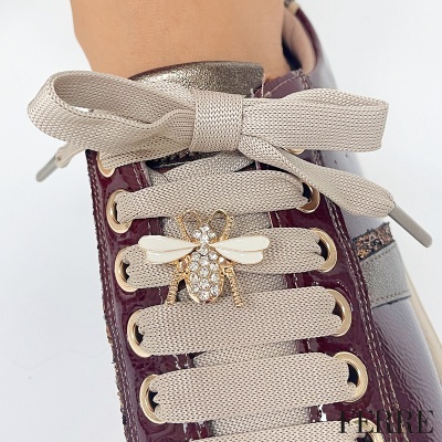 Tênis com atacadores bege e abelha decorativa dourada com pedras em fundo branco