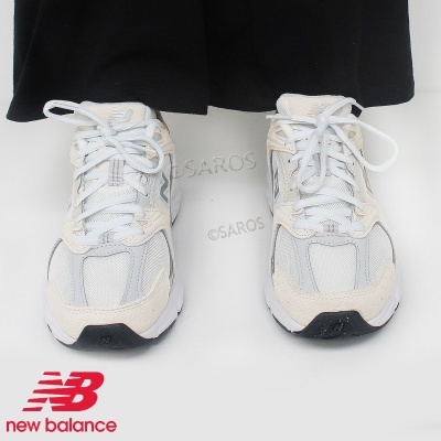 Ténis New Balance brancos e bege com sola branca, usados com calças pretas