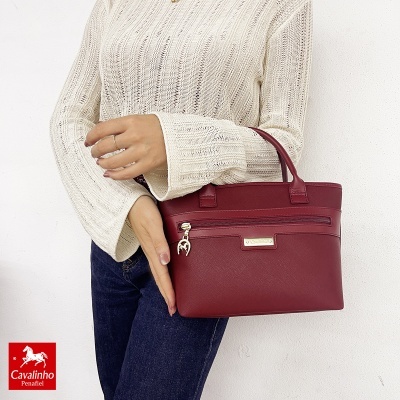 Mala de mão vermelha em pele sintética com bolso frontal e fecho, com pessoa a segurá-la