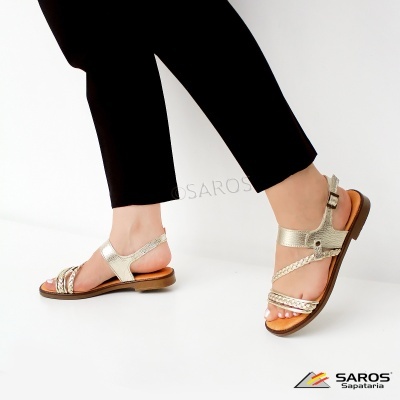 Sandálias douradas de couro com sola castanha e fecho de fivela, calçado em pé com calças pretas