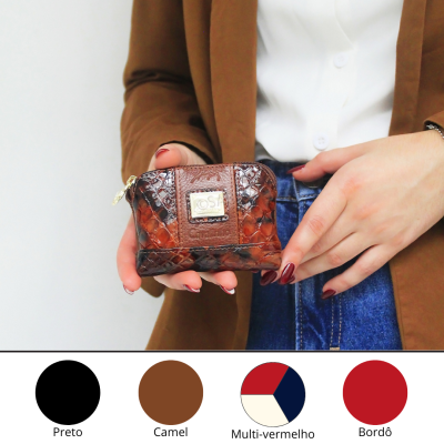 Carteira pequena de pele de cobra castanha com etiqueta metálica, segurada por pessoa com blazer camel e jeans azuis