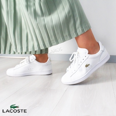 Tênis brancos com logo Lacoste em fundo interior com saia verde claro