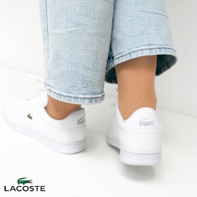 Ténis brancos Lacoste com logótipos e calças de ganga claras