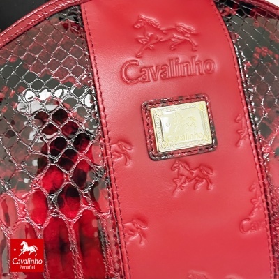 Detalhe de mala vermelha com padrão de pele de cobra, logo Cavalinho em relevo e placa dourada