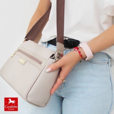 Mala bege claro com correia castanha usada por pessoa com pulseiras e calças de ganga