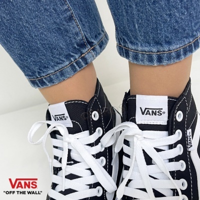 Ténis pretos Vans com atacadores brancos usados com jeans azuis