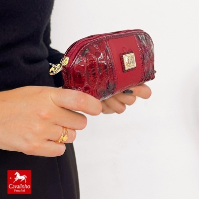 Carteira pequena vermelha de verniz com textura tipo pele, com fecho dourado, segurada por uma mão.